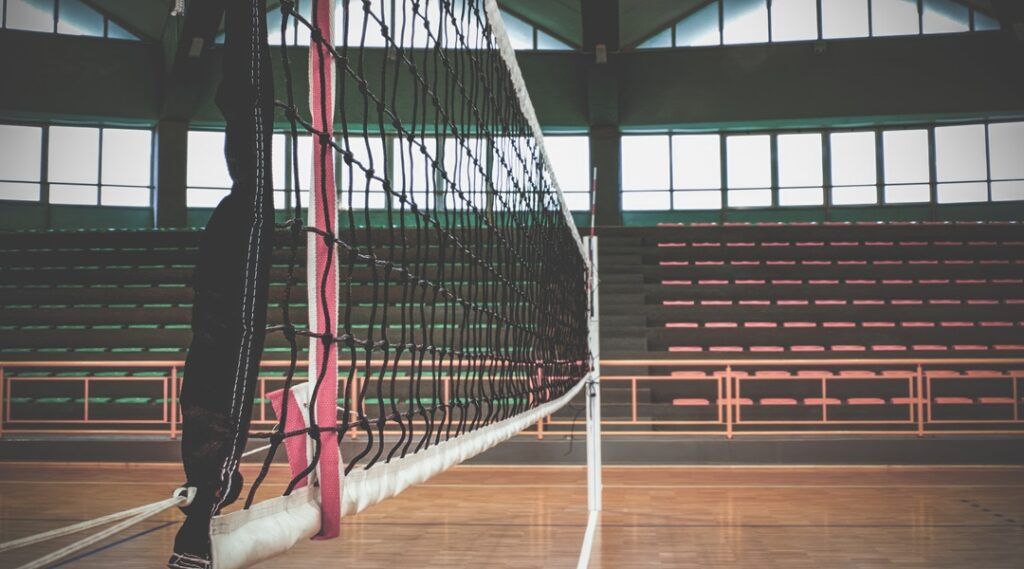 Volleyball net stands tall in empty gymnasium, ready for the game